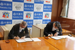 協定書に署名する奥塚市長（写真左）と岡村代表取締役